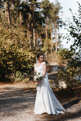 Fototapeta premium Bride in the wedding drees standing in the forest with her head titled to the shoulder