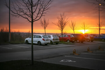 cars parked in small parking lot, disabled parking for handicapped or disabled car drivers with wheelchairs sign, sunset sky