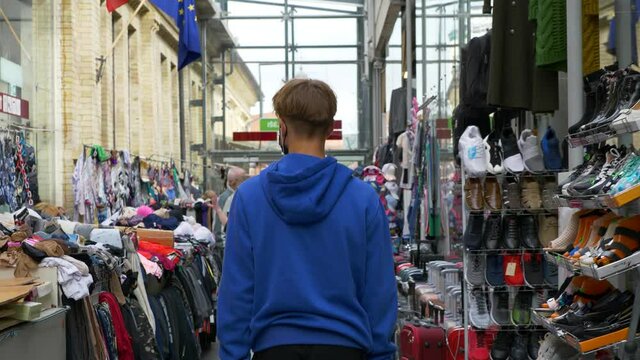 Slow motion shot of teenager walking through market full of clothes. Male filmed from back walking straight.
