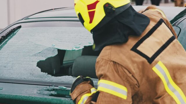 Car accident rescue, firefighter breaking the glass on the car. Close up, Slow motion shot.