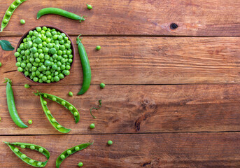 Fresh green peas in a bowl and pods on a rustic wooden table