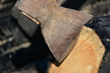 Close up of the blade of an old axe with a wooden handle stuck in a stump in the yard of a country...