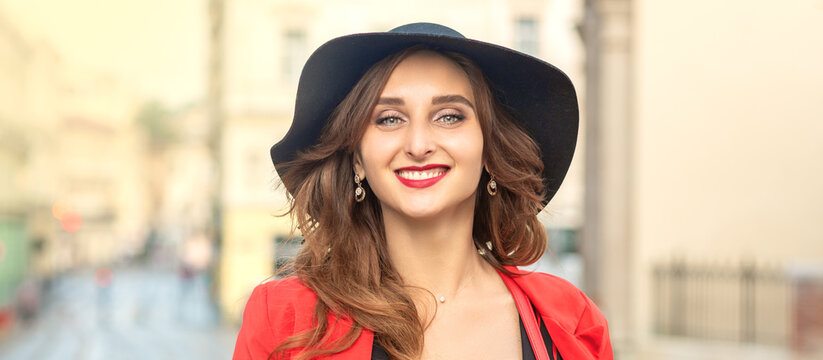 Outdoor portrait of young elegant fashionable woman wearing trendy hat walking in street of European city.