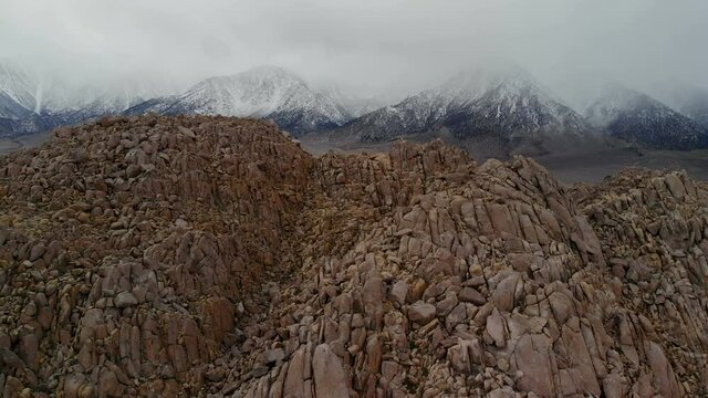 Aerial flyover through rugged boulders by alpine mountains in morning light at Alabama Hills, Eastern Sierra