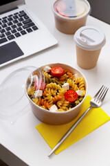 Food in taking away boxes on white table with laptop. Online food delivery