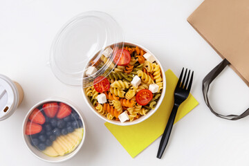 Pasta, coffee and fruits in taking away boxes on white table.