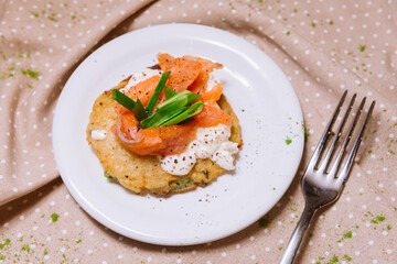Potato pancakes with red fish on top and green onions. A portion. Small plate.