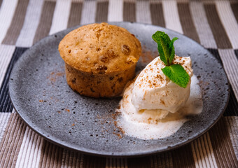 Carrot cake with a melted ball of cream ice cream decorated with mint leaves on a gray ceramic plate