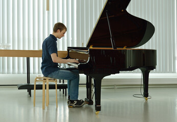 Young pianist playing on black grand piano in empty room
