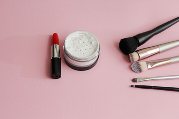 Obraz na płótnie Canvas makeup brushes, powder, red lipstick on a pink background
