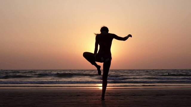 Young woman doing yoga assans on the beach at sunset background