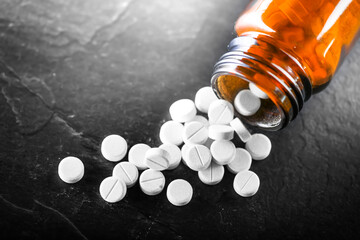 White medical pills or tablets with bottle on black background. Macro side view with copy space