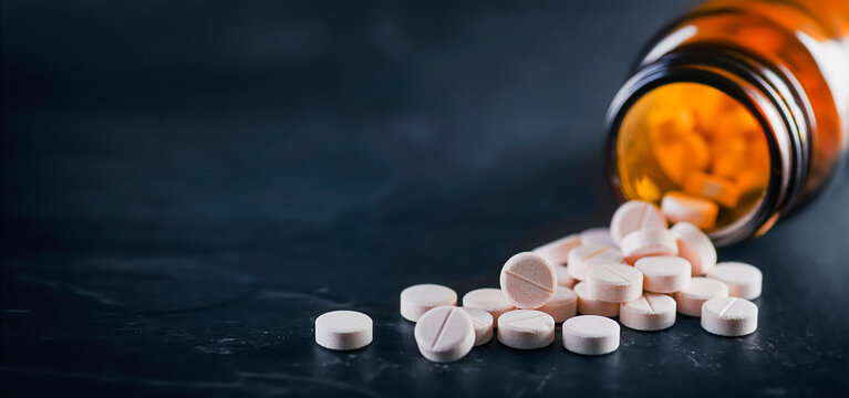 White medical pills or tablets with bottle on black background. Macro side view with copy space
