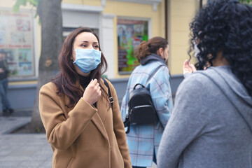 beautiful ladies talking on the street, wearing medicine masks due to coronavirus, protection from the virus, keeping the distance