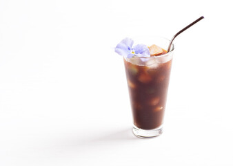 A glass with cold coffee and ice cubes stands on a white background. Iced coffee is decorated with an edible flower. Horizontal orientation, there is a copy space.