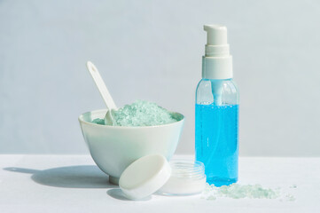 Obraz na płótnie Canvas Blue gel in a bottle, white cup, blue bath salt, cream in a jar on a white background.