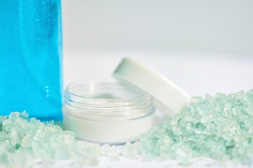 Blue gel in a bottle, white cup, blue bath salt, cream in a jar on a white background.