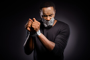 Photo of furious mad afro american guy restrained adhesive tape hand lips close cover suffer no talking speaking injustice isolated over black color background