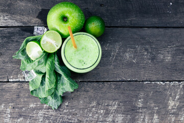 Green apple smoothie in glass and kale leaves on wooden table
