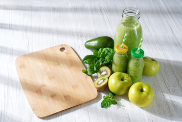 Detox juice. Summer green smoothie on the white wooden table. Drink made with green fruits, vegetables and greenery.