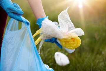 Faceless portrait of person picking up rubbish, wearing latex blue disposable glove, holding litter in hands, cleaning field, takes care of planet ecology.