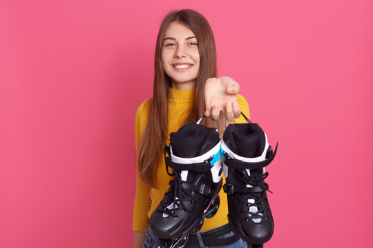 Caucasian smiling lady holding roller skates, showing her sports equipments, looking directly at camera, spending time in active way, lady expressing positive emotions.