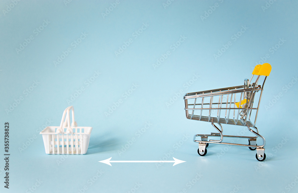 Wall mural miniature shopping trolley and white basket isolated on blue background with copy space. empty minia