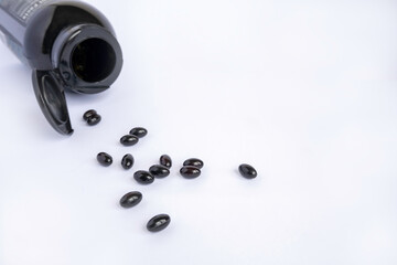 Dark astaxanthin capsules next to a can of vitamins on a light background. Vitamins and supplement for healthy life and energy.