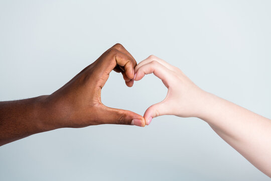 Closeup photo of two hands arms different race skin color multinational couple best friends anti racism issue help together showing heart figure love save world isolated grey background