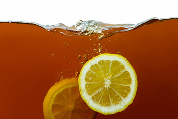 Closeup process of making black tea. Macro shot of dipping, falling pieces, wedges of yellow lemon into transparent glass cup. Splashes, waves, sprays of liquid. Hot drinks, beverages concept.