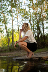 Girl near the water. A blonde woman in a white shirt poses on the Bank of a river or lake.