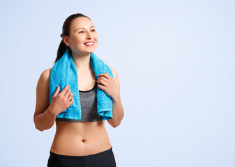 Fototapeta na wymiar Happy young fitness woman in sports clothes with a towel on her shoulders on a blue background