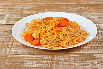 Pasta with carrots in a white plate on a wooden table. Vermicelli with orange sauce on a pink shabby board.