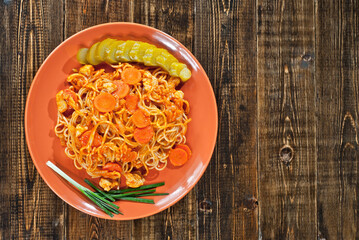 Pasta with carrots, cucumber and onion plate on a wooden table. Vermicelli with orange sauce on a black shabby board. Place for text near the plate. Copy space for design.