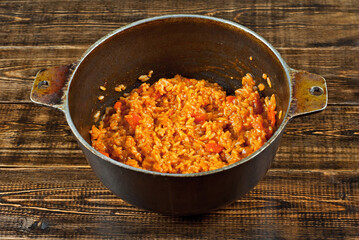 Pilaf with meat and carrots in an old cast iron cauldron. Rice on a brown shabby board.