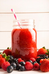 Beautiful healthy red raspberries, blackberry, strawberry and blueberry fruit smoothie in glass jar with fresh berries background with paper straw
