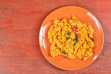 Pilaf with meat, cucumbers, greens and carrots in an orange plate. Rice on wooden red plywood. Place for text and copy space near food.