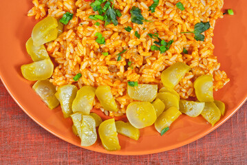 Pilaf with meat, cucumbers, greens and carrots in an orange plate. Rice on wooden red plywood.