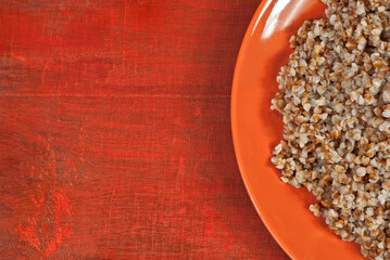 Buckwheat orange plate on a wooden table. Food in utensils on a background of old red plywood. Place for text near the plate. Copy space for design.