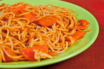 Pasta with carrots in a green plate on a wooden table. Vermicelli with orange sauce on red plywood.