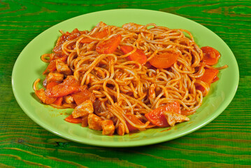 Pasta with carrots and meat in a green plate on a wooden table. Vermicelli with orange sauce on a shabby board.