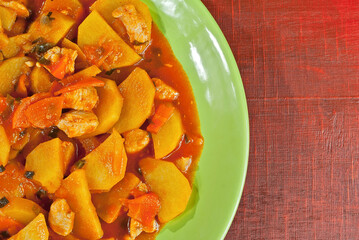 Potatoes in a green plate on a wooden table. Boiled potatoes with orange sauce on a red board. Place for text near the plate. Copy space for design.