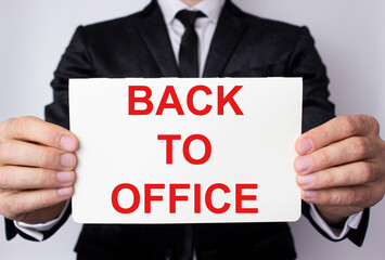 Back to office is written on a white sheet held by a businessman in a business suit.