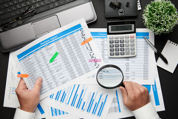 Top view of businessman's hands working with financial reports. Modern black office desk with...