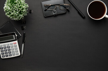 Top view of modern black office desk with calc, notebook, pen and a lot of things. Flat lay table layout. Copy space for text.