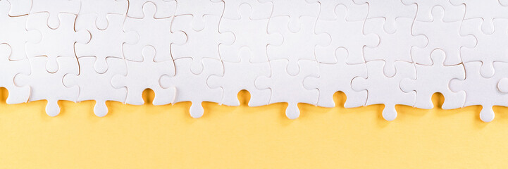 Assembled white jigsaw puzzle pieces on yellow long panoramic background