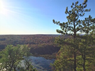 View over the edge of a cliff on a mountain on Lantern Hill trail in Connecticut, with a pond below in the distance 