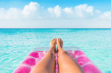 Summer relax vacation woman pov of legs relaxing on pink inflatable pool toy float floating in turquoise water ocean background. Suntan at tropical beach. - obrazy, fototapety, plakaty