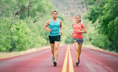 Obraz premium Summer run man and woman runners couple fit people jogging training for marathon. Young athletes on fast cardio jog workout in summer park road.