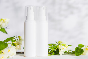 Fototapeta na wymiar Unbranded skincare products plastic bottle with dispenser and flacons. Tube for cream shampoo. Green jasmine flowers and their shadows on the white background isolated. Mockup and copy space